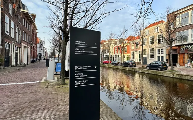 Informatiezuil met bewegwijzering aan de gracht bij Hotel Arsenaal in Delft