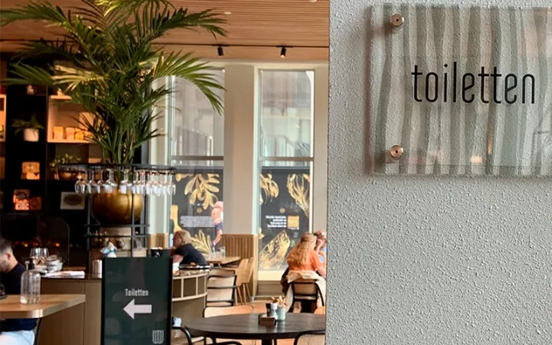 Glazen bordje toiletten aan de wand en een verwijsbord in de restaurantruimte