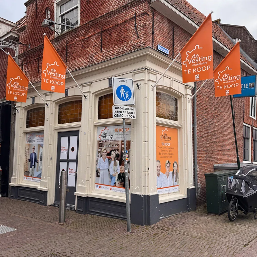 Hoekpand met oranje te-koop-vlaggen en raamreclame van Vesting Makelaars