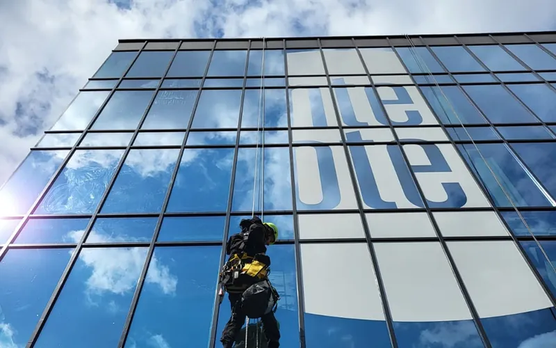 Abseiler werkt aan een grote raamsticker op een glazen gevel