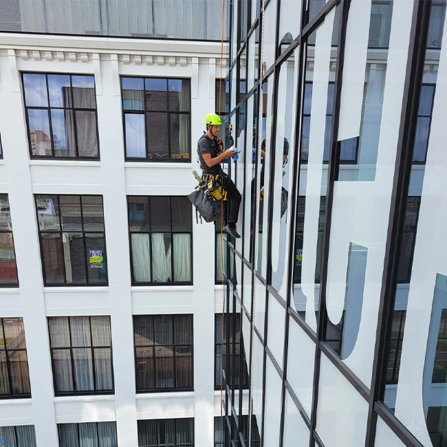 Stickers aanbrengen abseilers hoogtewerk abseiltechniek gebouwbelettering