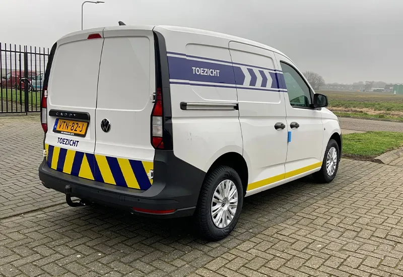 Witte bestelbus met blauwe toezicht-belettering en geel-zwarte chevrons op de achterdeuren