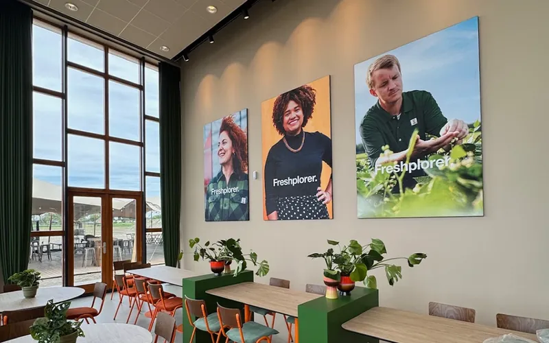 Drie textielframes met portretten aan de wand van een bedrijfsrestaurant