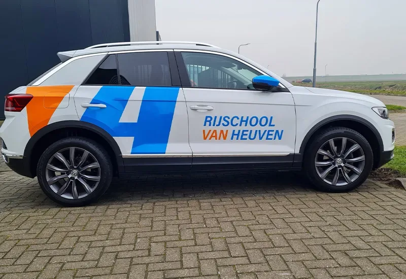 Witte Volkswagen T-Roc met blauw-oranje huisstijlvlakken en de tekst Rijschool van Heuven