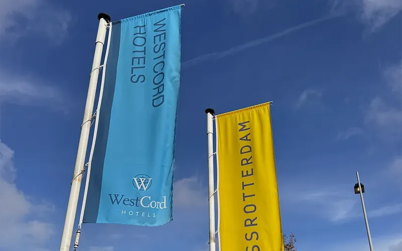Banieren van WestCord Hotels aan vlaggenmasten tegen een blauwe lucht