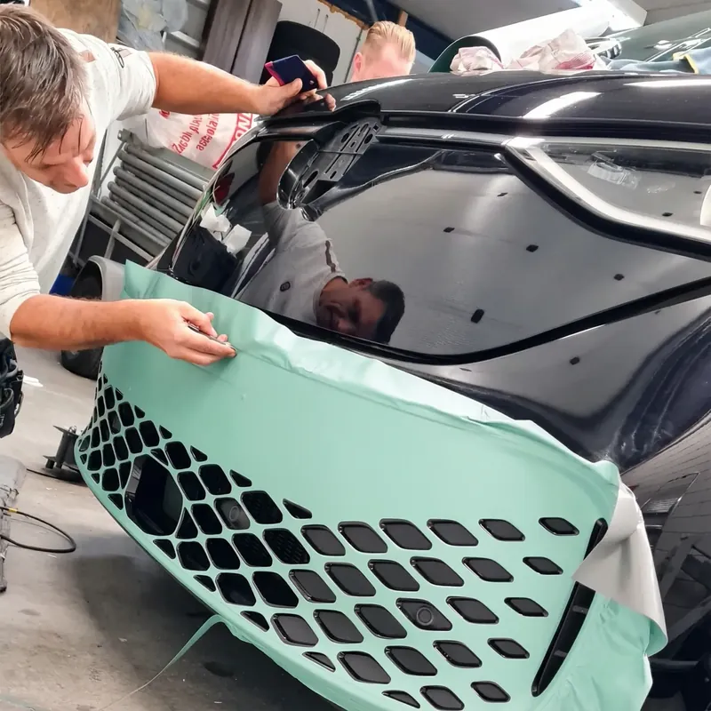 Monteur legt mintgroene folie op de voorbumper van een auto in de werkplaats