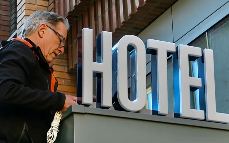 Monteur werkt aan witte doosletters HOTEL op een gevel