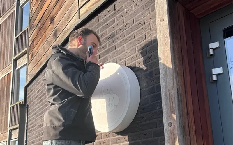 Monteur bevestigt een rond lichtbakje aan een bakstenen gevel