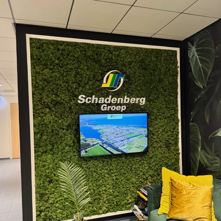 Bedrijfsnaam in witte 3D-letters op een moswand met scherm in de ontvangstruimte
