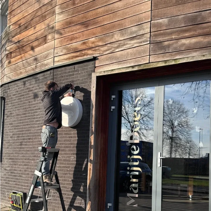 Monteur hangt een rond wit lichtbakje aan de gevel vanaf een trap