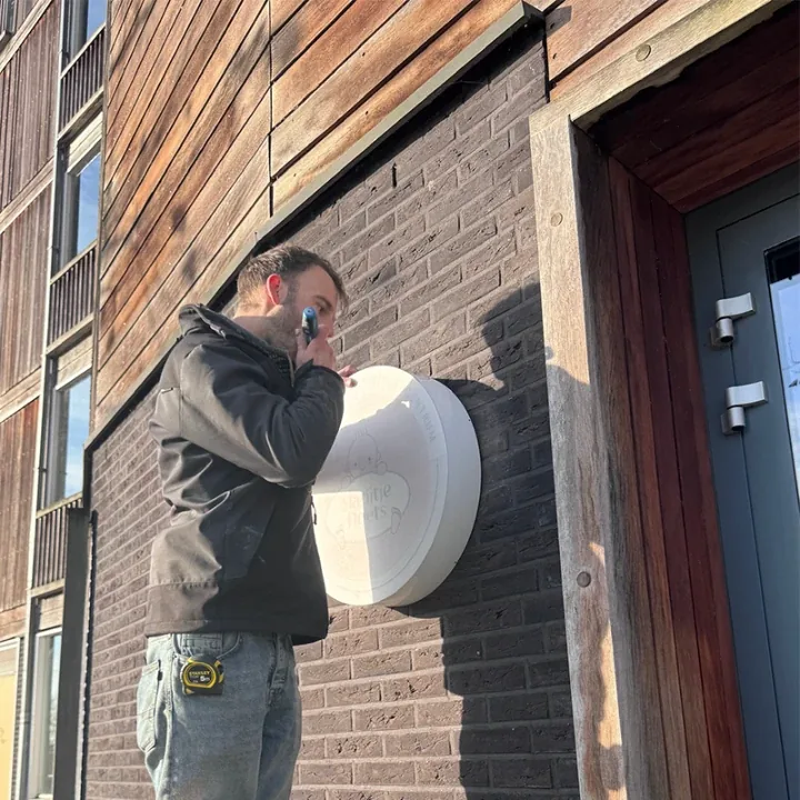 Monteur boort het ronde lichtbakje vast op de bakstenen gevel
