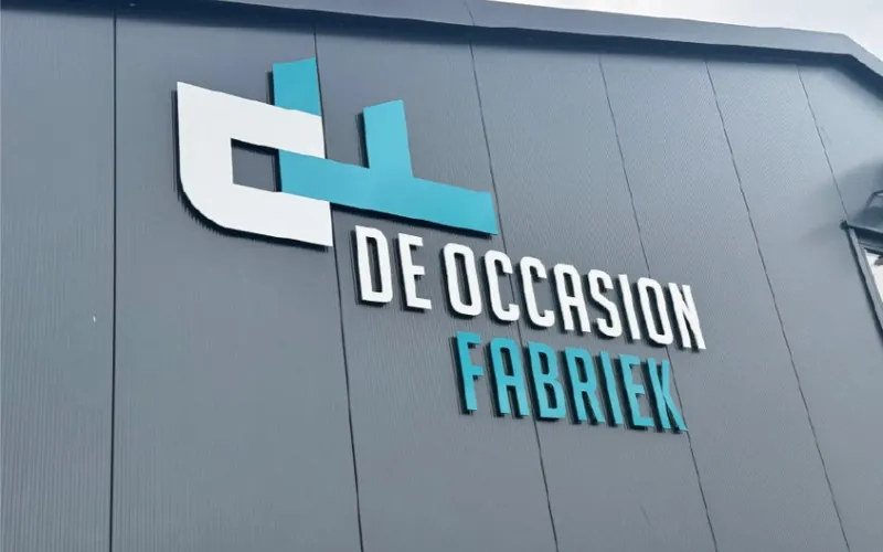Onverlichte freesletters met logo op een grijze gevel bij daglicht