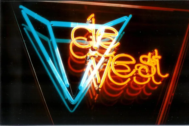 Blauw en oranje handgeblazen neonlogo van De Vest, weerspiegeld in een spiegel