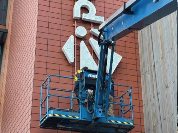 Hoogwerker bij grote witte letters op een rode gevel tijdens de montage
