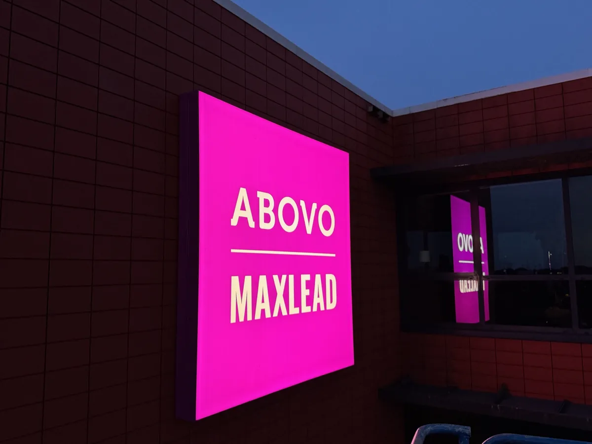 Roze verlichte lichtbak ABOVO MAXLEAD op de donkere gevel bij avond