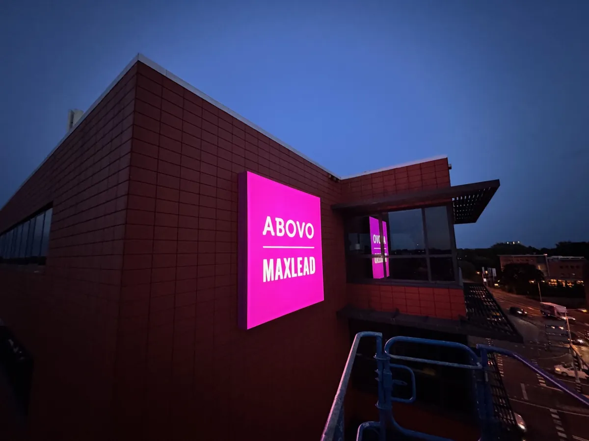 Roze verlichte lichtbak ABOVO MAXLEAD op de hoek van het rode kantoorpand bij schemer
