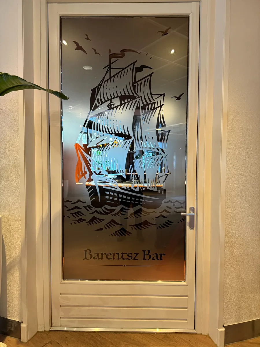 Glazen deur met een zandstraalfolie-afbeelding van een zeilschip en de tekst Barentsz Bar