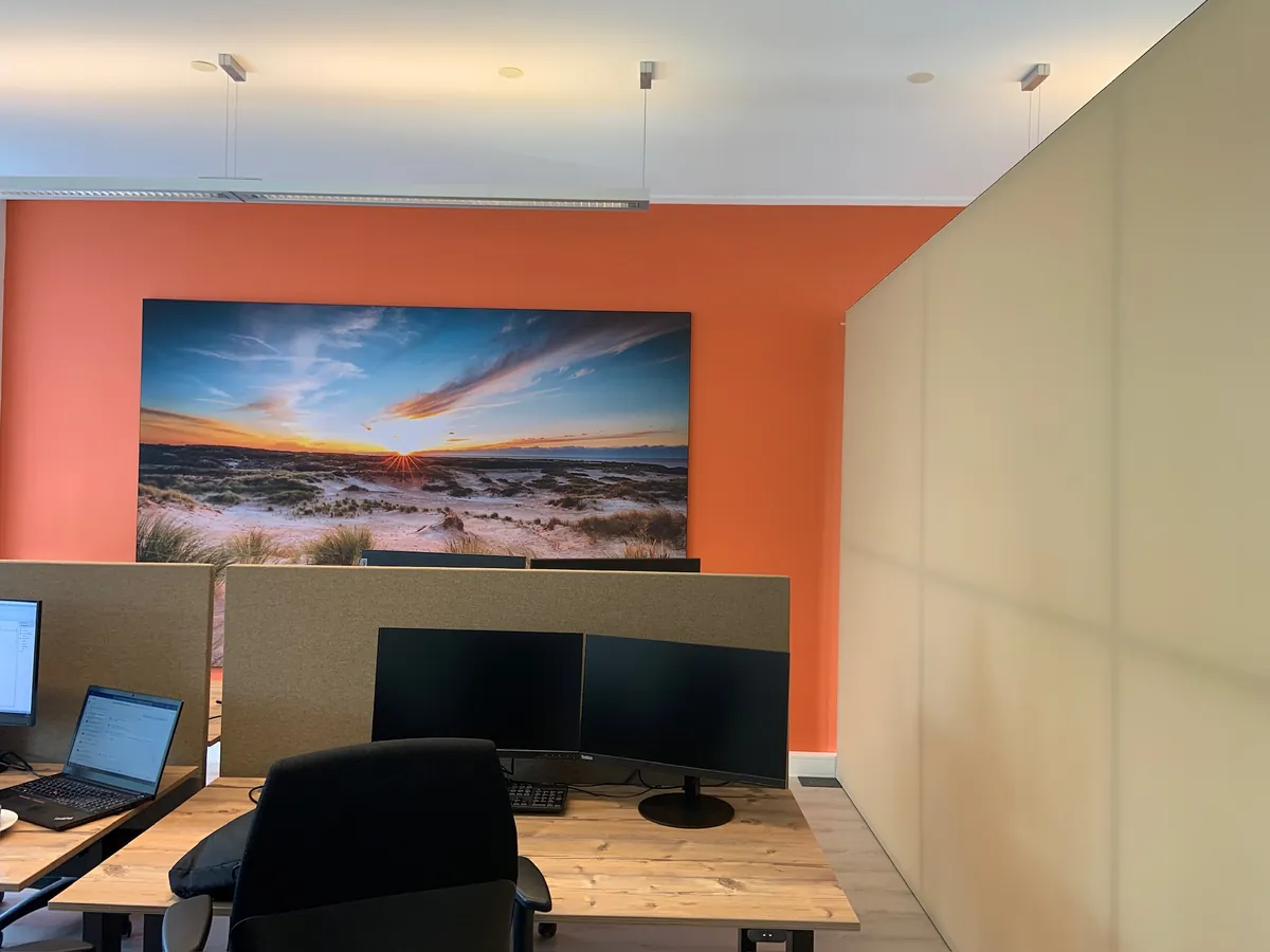 Print van duinen bij zonsondergang op een oranje wand boven een werkplek