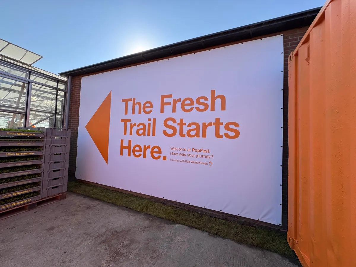 Groot spandoek met een oranje pijl en de tekst The Fresh Trail Starts Here aan een containerwand