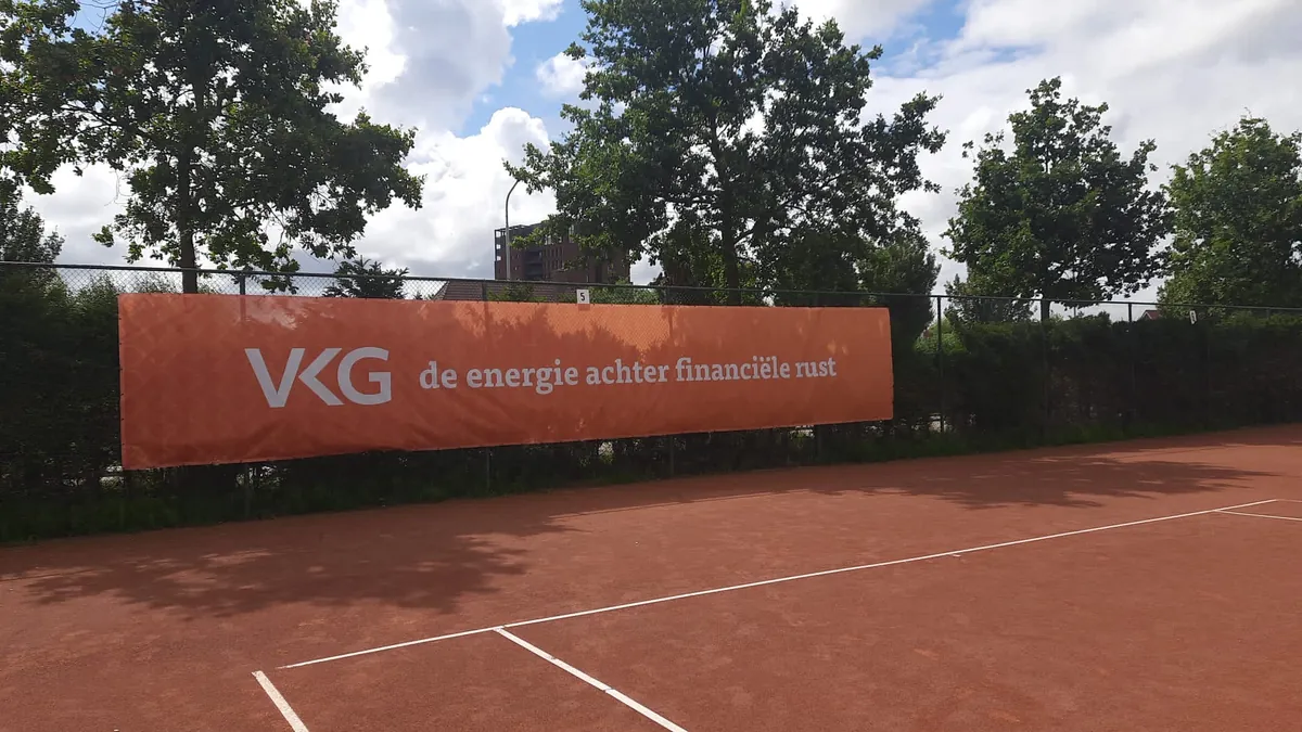 Oranje reclamedoek van VKG langs een gravel tennisbaan
