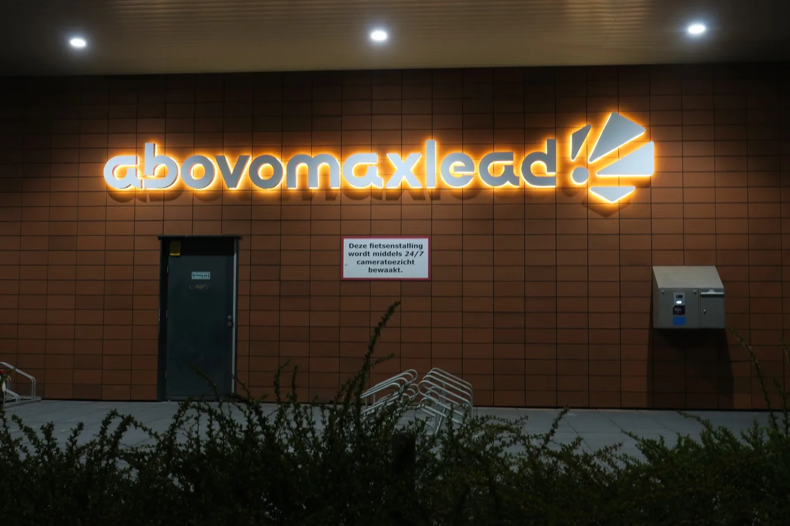 Oranje verlichte letters en logo van Abovomaxlead op de bakstenen gevel in het donker