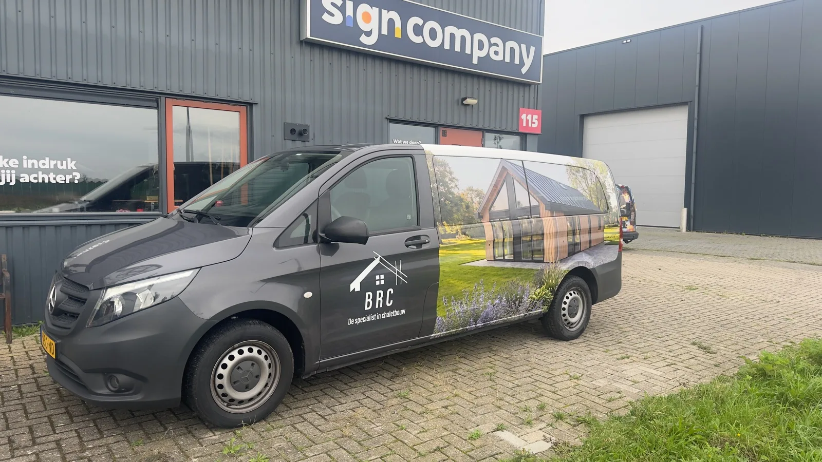 Grijze bus van BRC met logo en beeld van een huis op de zijkant, voor de werkplaats