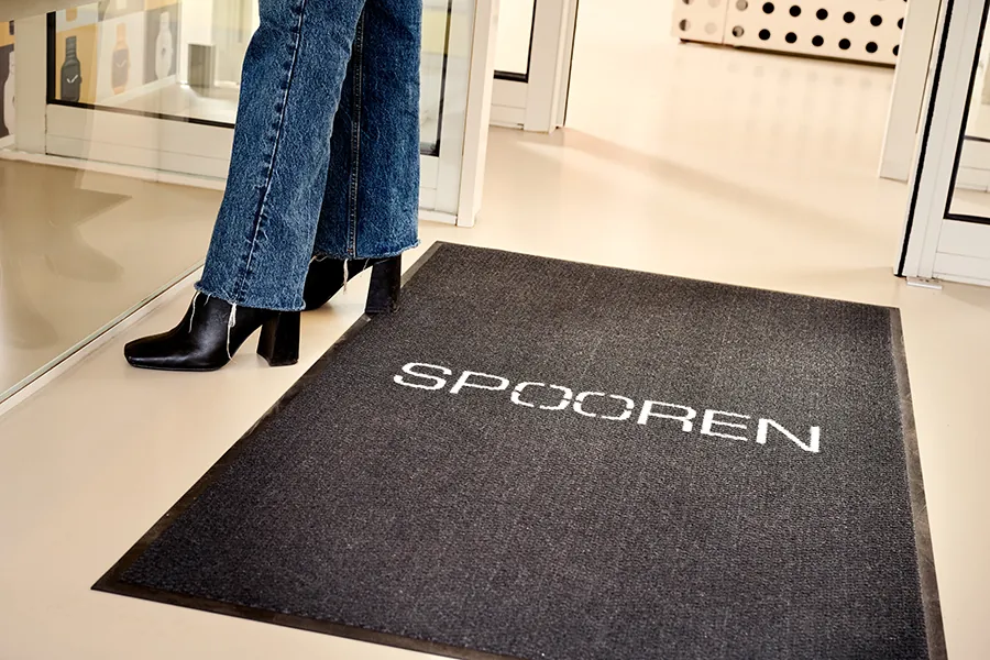 Donkere schoonloopmat met bedrijfsnaam in de entree van een winkel