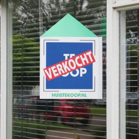 Makelaarsbord als sticker tegen het raam, verkocht