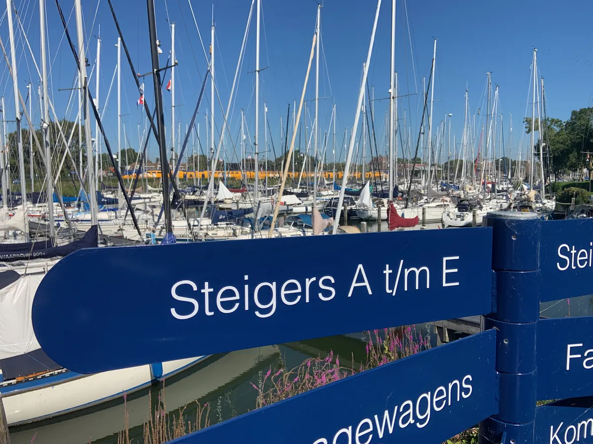 Blauwe wegwijzerarmen met Steigers A t/m E, zeilboten erachter