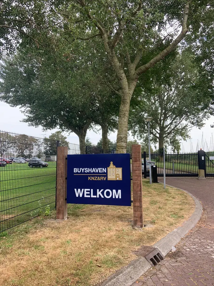 Blauw welkomstbord van Buyshaven tussen twee houten palen bij de ingang