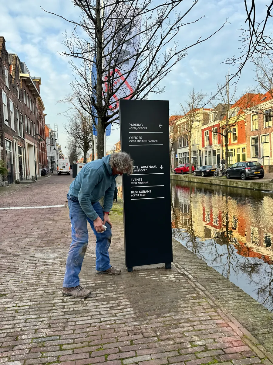 Monteur zet een bewegwijzeringszuil vast aan de gracht