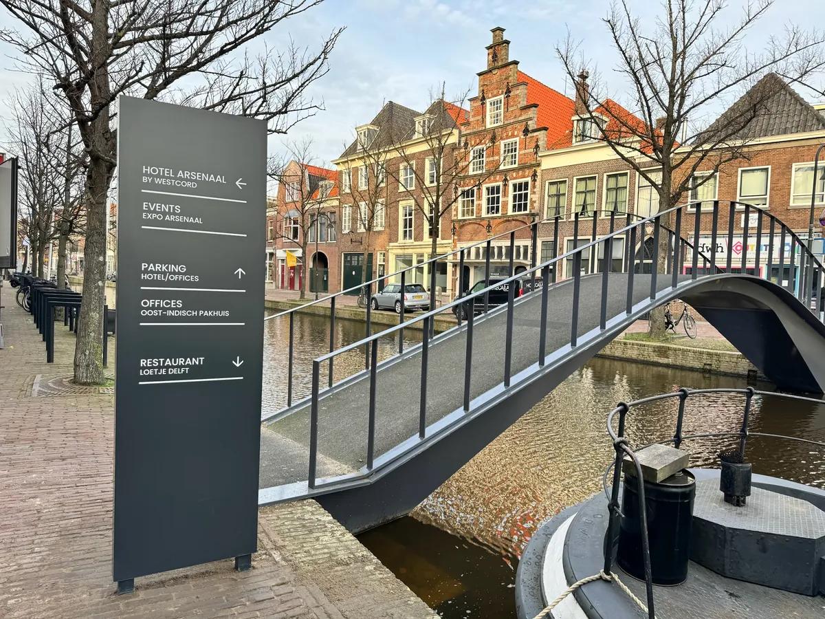Donkere bewegwijzeringszuil van Hotel Arsenaal naast een brug over de gracht