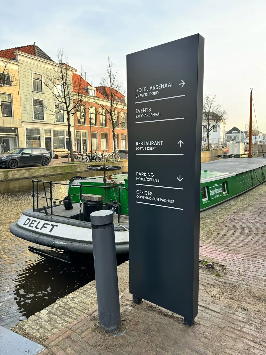 Donkere bewegwijzeringszuil van Hotel Arsenaal aan de gracht