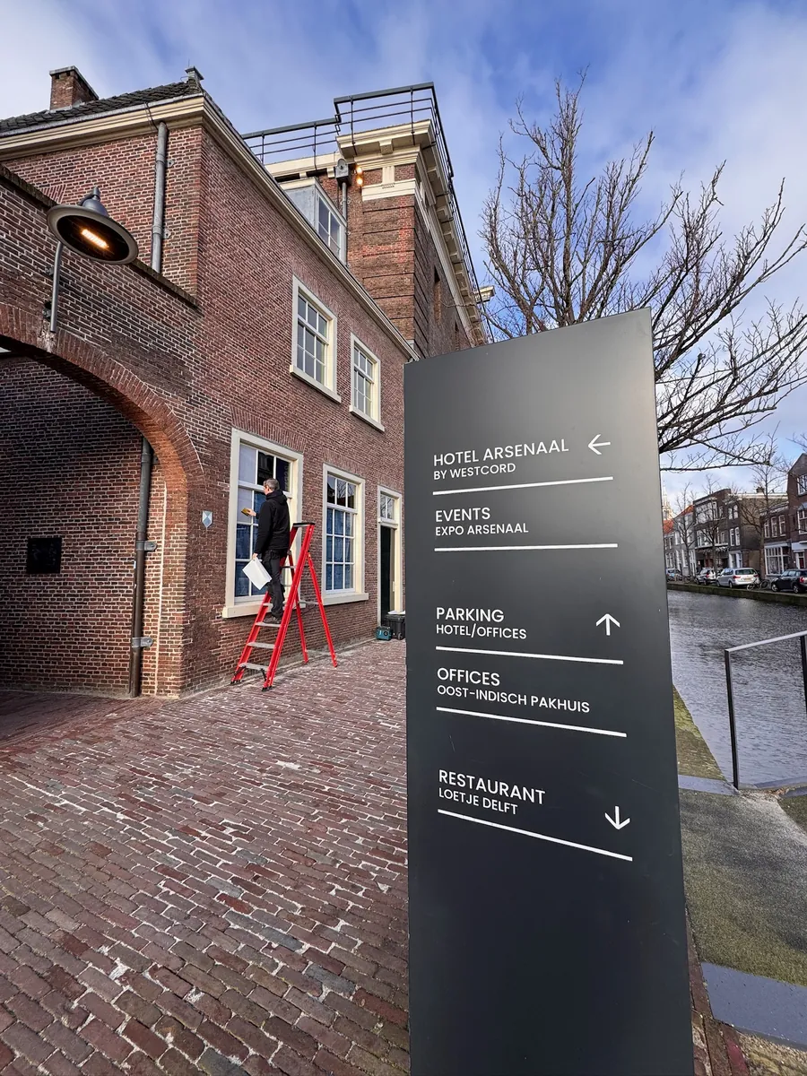 Bewegwijzeringszuil voor het bakstenen pand, met een monteur op een ladder op de achtergrond