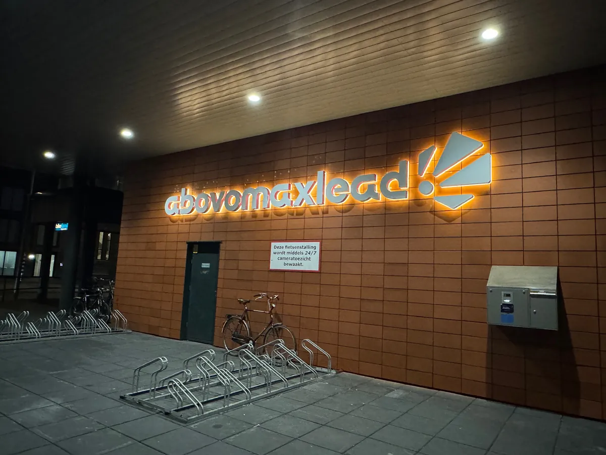 Letters abovomaxlead met halo-verlichting op de bakstenen gevel bij de fietsenstalling