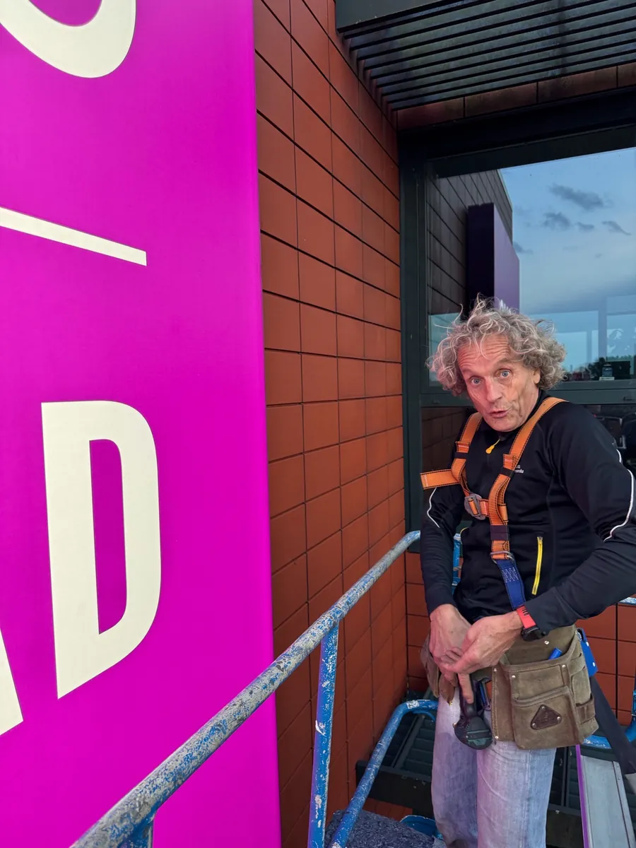Monteur in klimgordel op een hoogwerker naast het grote roze gevelbord