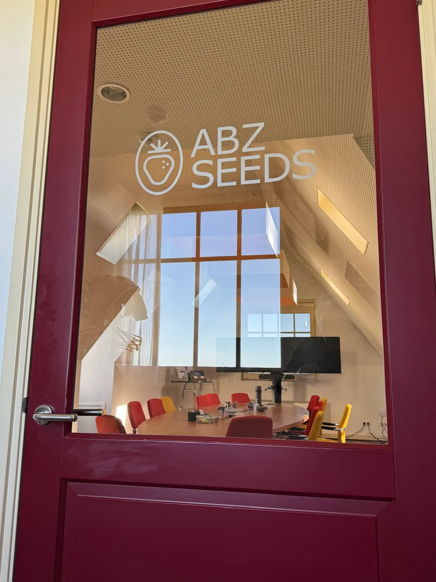ABZ SEEDS-logo op het glas van een donkerrode deur, met een vergaderruimte erachter