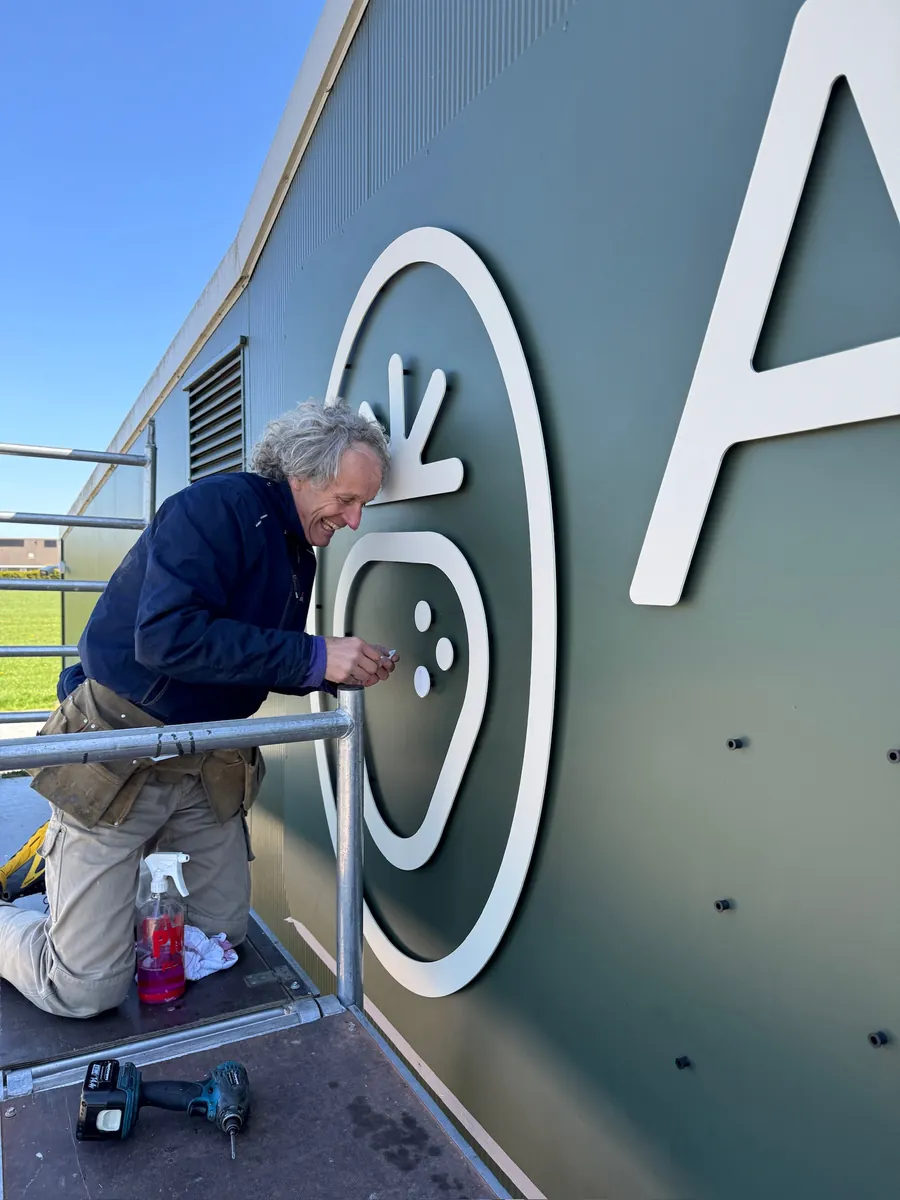 Monteur op een steiger bevestigt het witte ABZ-beeldmerk op de groene gevel