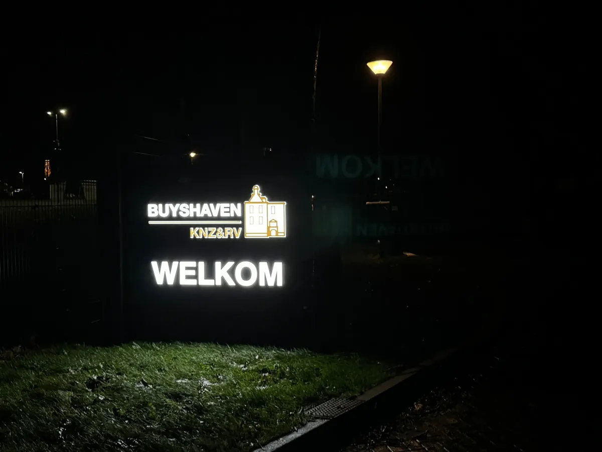 Verlicht welkomstbord van Buyshaven in het gras, in het donker