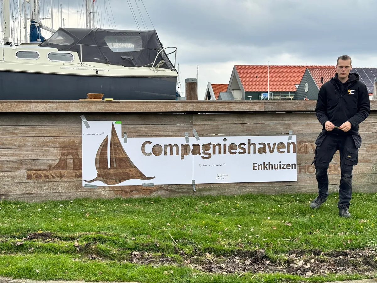 Monteur naast het houten bord met het Compagnieshaven-logo bij de haven