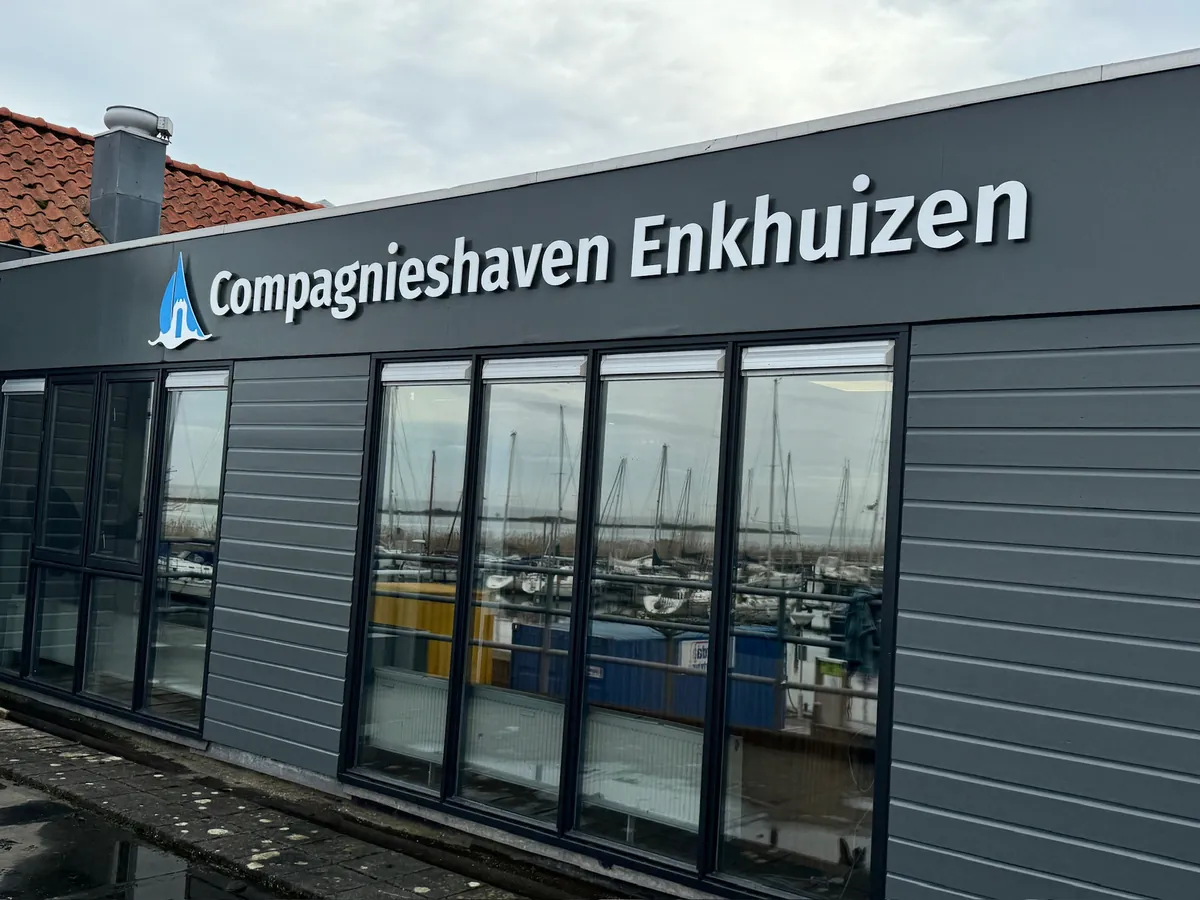Logo en letters Compagnieshaven Enkhuizen op de grijze gevel van het havengebouw