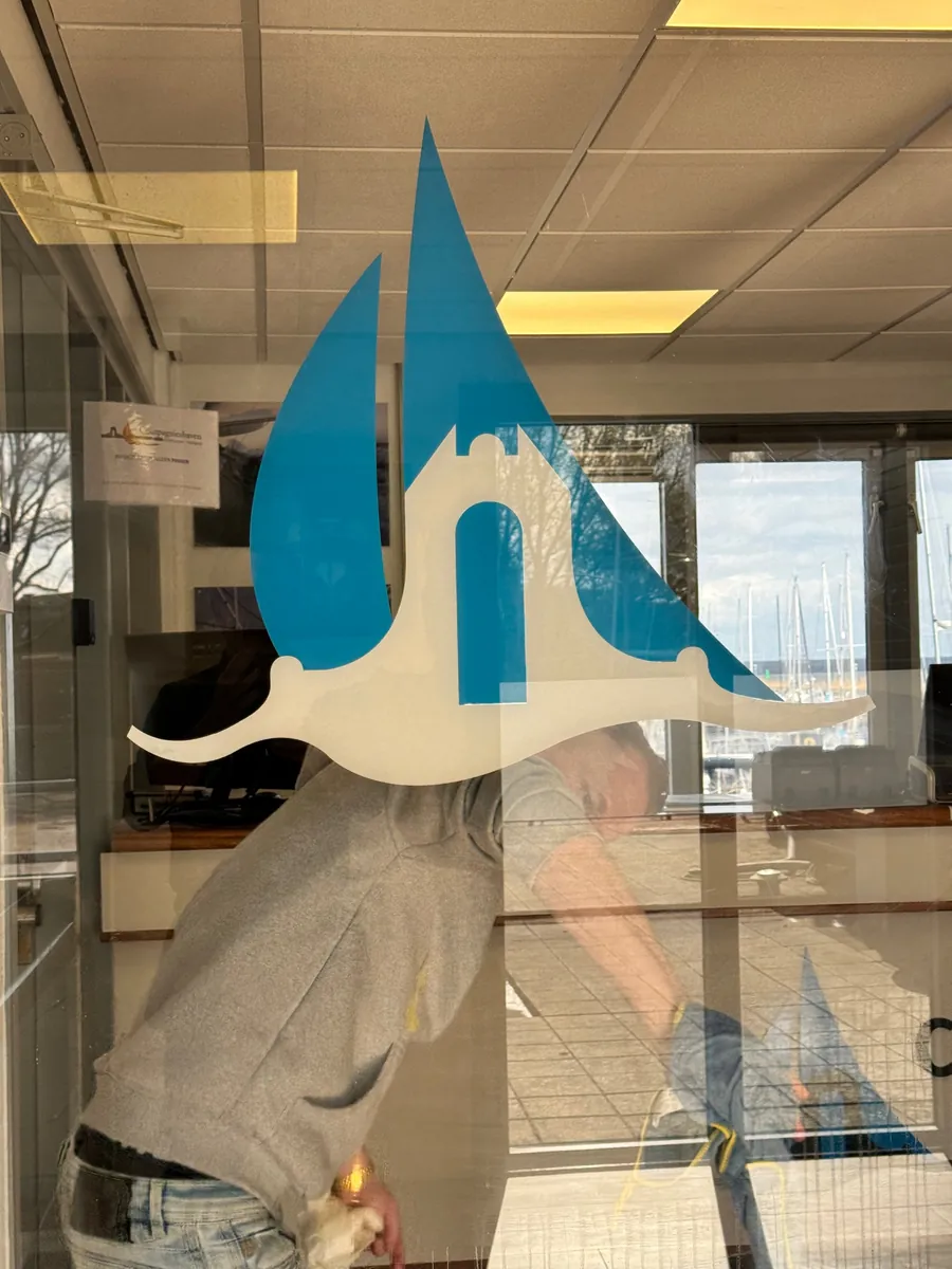Monteur plakt het blauwe logo van Compagnieshaven op een glazen deur