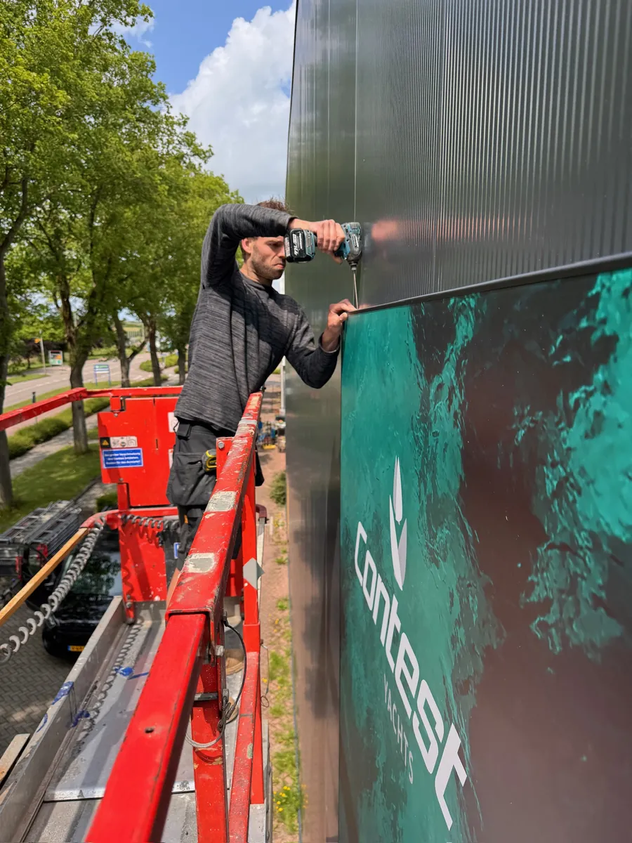 Monteur op een hoogwerker zet het groene gevelbeeld vast