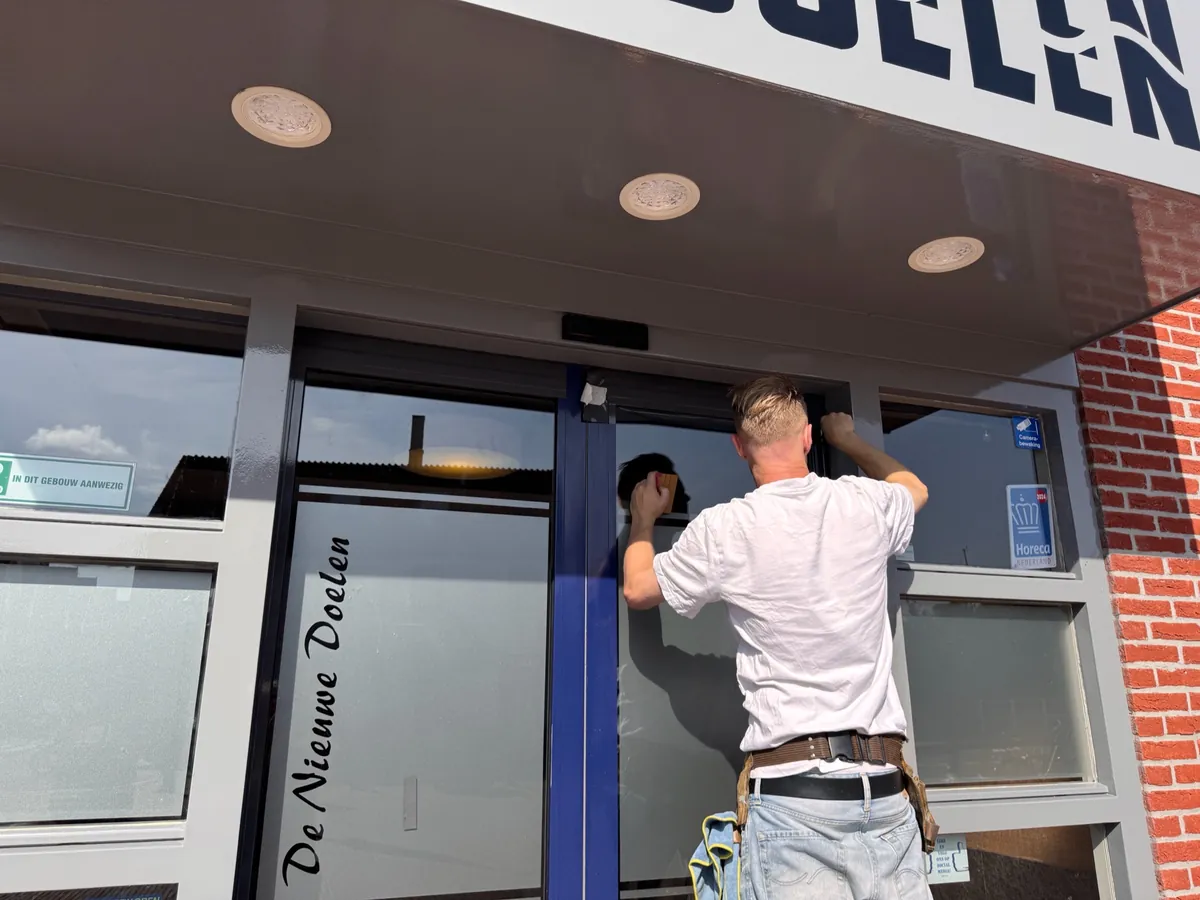 Monteur plakt raamfolie op het glas van de entreedeur onder het naambord