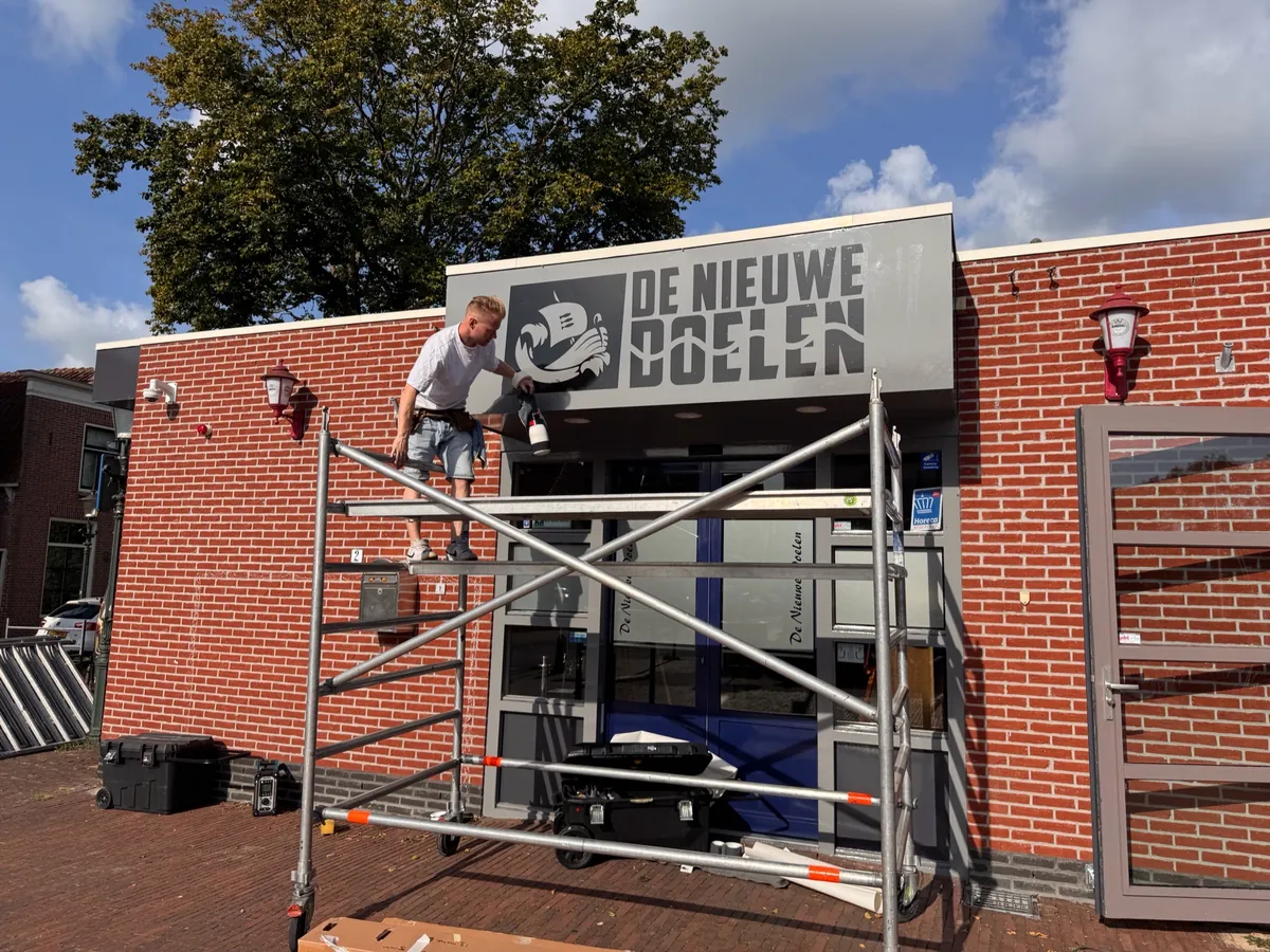 Monteur op een rolsteiger bij het naambord DE NIEUWE DOELEN