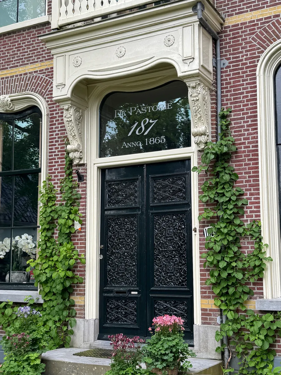 Letters DE PASTORIE boven de sierlijke voordeur van een historisch pand met klimop