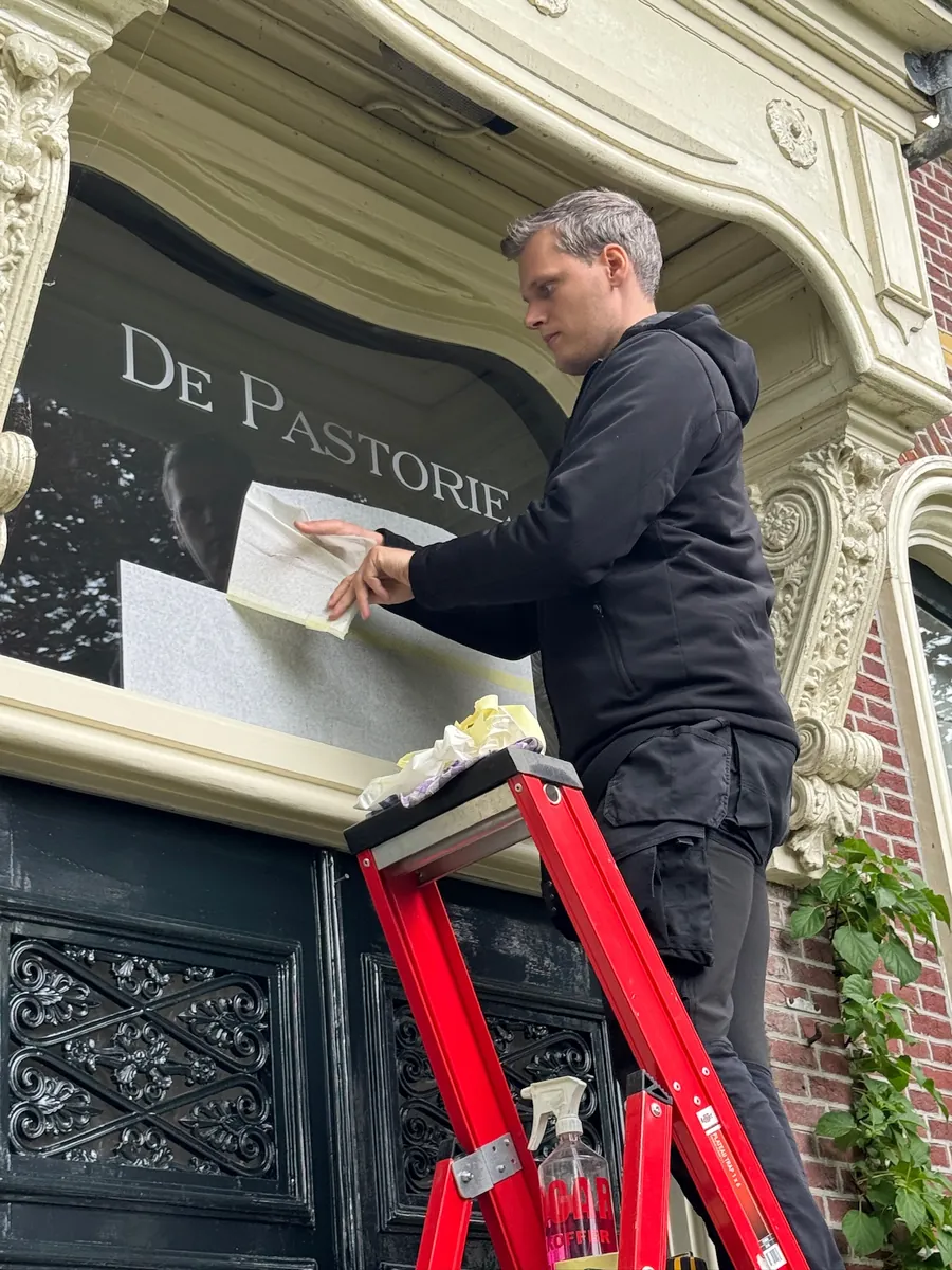 Monteur op een rood trapje brengt de letters De Pastorie aan boven de voordeur