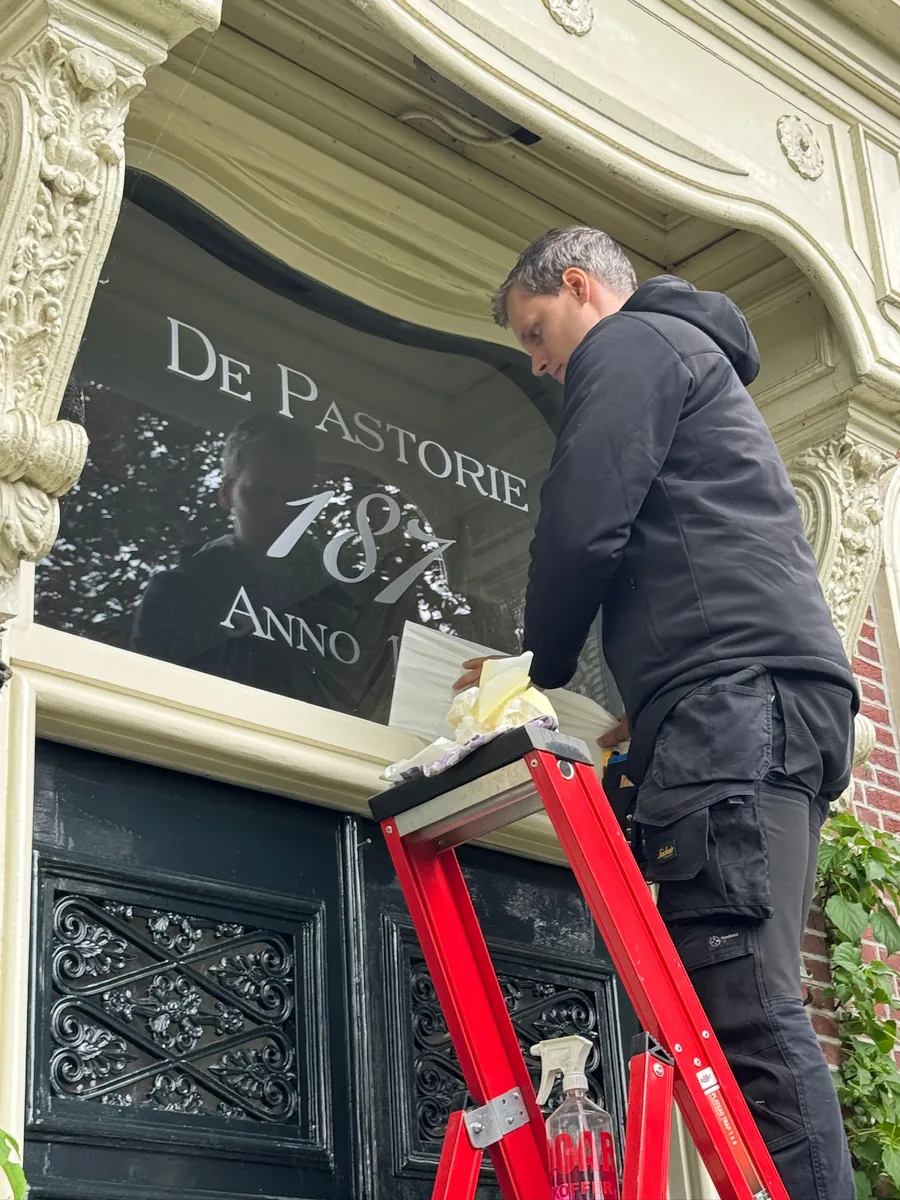 Monteur werkt de letters De Pastorie op het glas boven de deur af