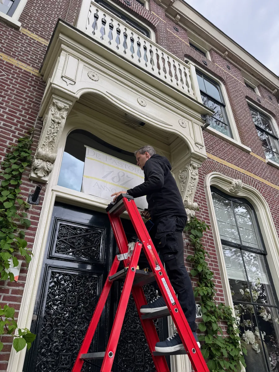 Monteur op een rode trap bij het bovenlicht boven de voordeur