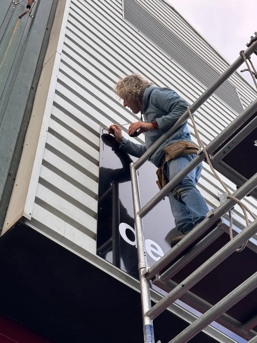 Monteur op een rolsteiger bevestigt het gevelbord op de lichte gevelbeplating